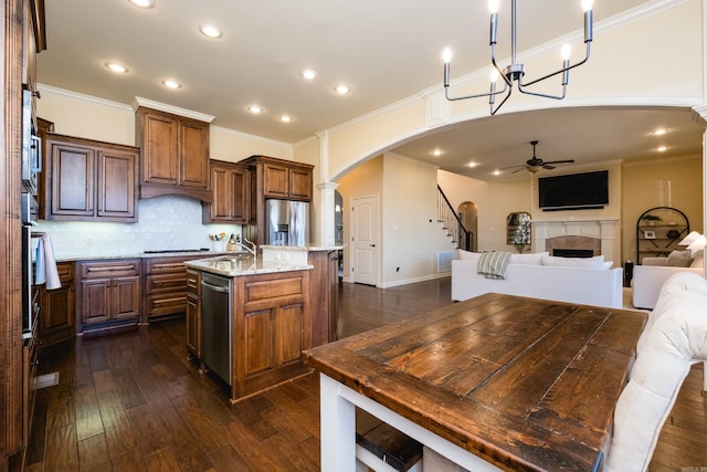 kitchen featuring a kitchen island with sink, a tiled fireplace, arched walkways, appliances with stainless steel finishes, and ceiling fan