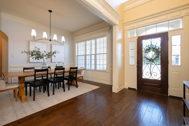 foyer entrance featuring ornamental molding, dark wood finished floors, an inviting chandelier, wainscoting, and a decorative wall