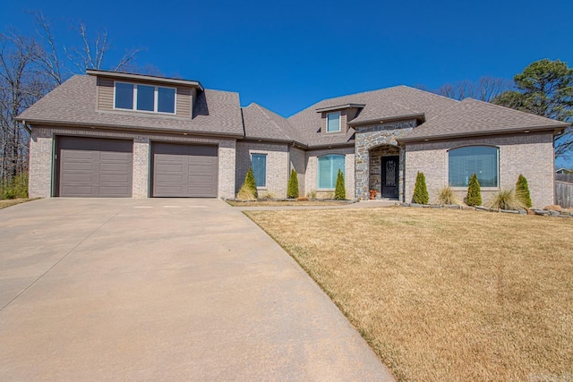 view of front of property featuring driveway, roof with shingles, a front yard, a garage, and brick siding