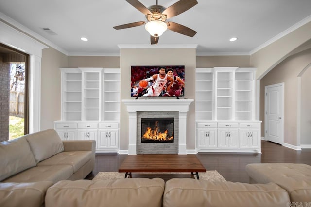 living room featuring dark wood finished floors, a stone fireplace, ceiling fan, and ornamental molding