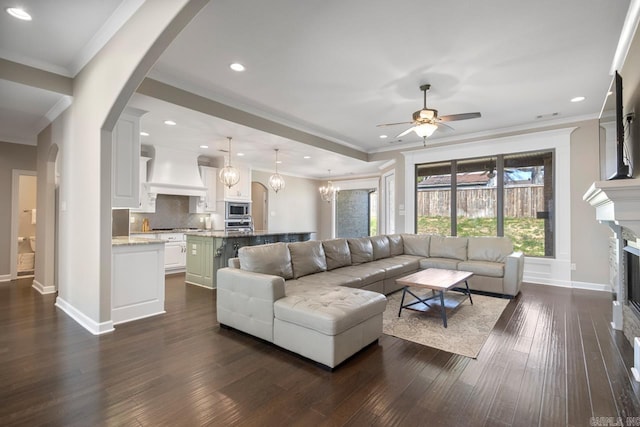 living area with a glass covered fireplace, baseboards, dark wood finished floors, and a ceiling fan