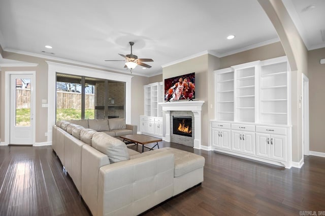 living room with arched walkways, a ceiling fan, dark wood-style flooring, and a lit fireplace