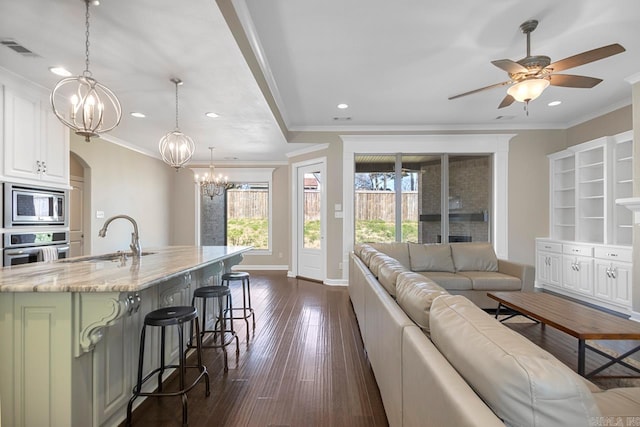 living area with visible vents, dark wood-style floors, ornamental molding, and ceiling fan with notable chandelier