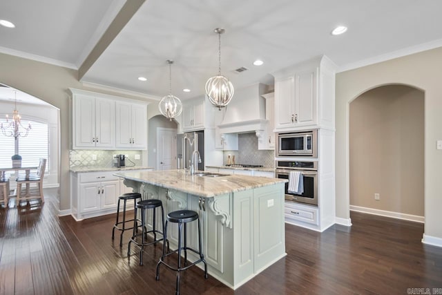 kitchen with a sink, arched walkways, appliances with stainless steel finishes, custom exhaust hood, and a chandelier