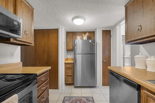 kitchen with a textured ceiling, appliances with stainless steel finishes, brown cabinetry, light countertops, and light tile patterned floors