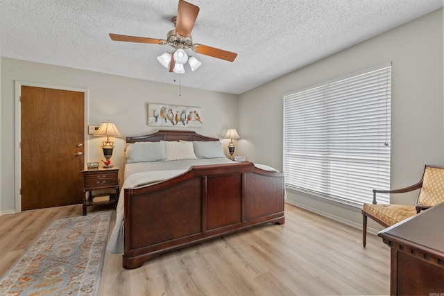 bedroom featuring ceiling fan, baseboards, light wood finished floors, and a textured ceiling