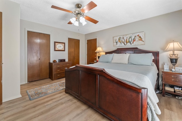 bedroom with two closets, a ceiling fan, light wood finished floors, and a textured ceiling