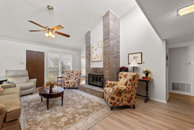 living area featuring visible vents, wood finished floors, a brick fireplace, ceiling fan, and vaulted ceiling