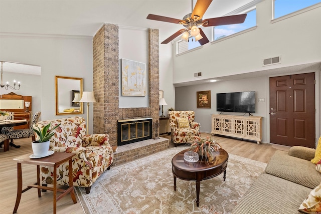 living room with visible vents, wood finished floors, a fireplace, and ceiling fan with notable chandelier