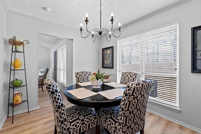 dining space featuring baseboards, ornamental molding, a textured ceiling, light wood-type flooring, and a chandelier