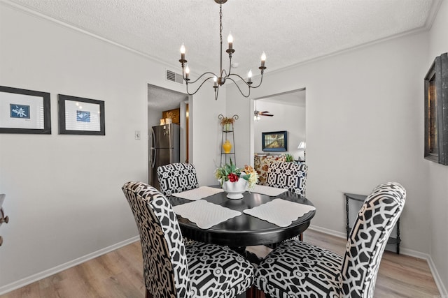 dining area with visible vents, a notable chandelier, light wood-style flooring, ornamental molding, and a textured ceiling