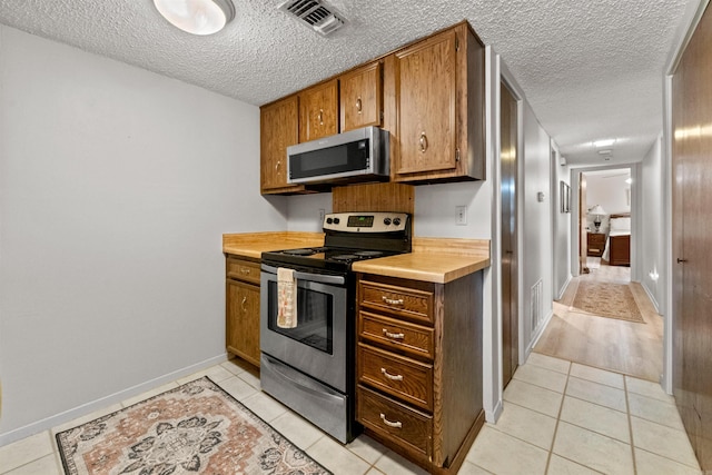 kitchen with visible vents, light tile patterned floors, stainless steel appliances, brown cabinetry, and a textured ceiling