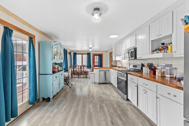 kitchen with open shelves, ornamental molding, appliances with stainless steel finishes, white cabinetry, and light wood-type flooring