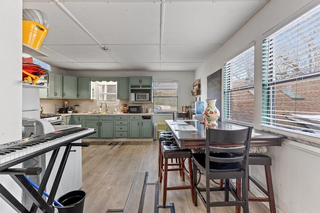 kitchen featuring green cabinetry, light countertops, light wood-type flooring, decorative backsplash, and a sink