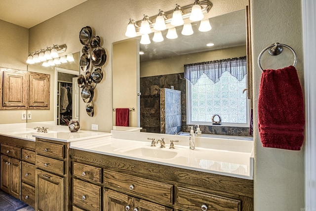 full bathroom with double vanity, a tile shower, a textured wall, and a sink