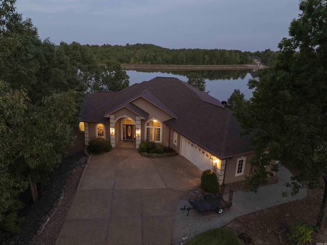 view of front of home featuring a forest view, a shingled roof, a water view, a garage, and driveway