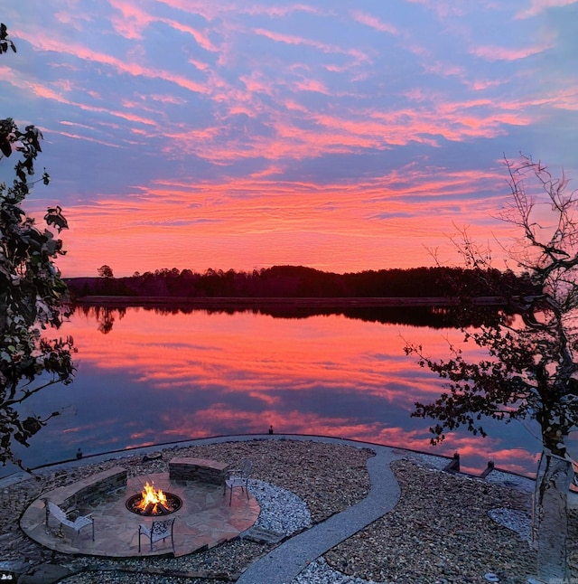 yard at dusk with a patio, a fire pit, and a water view