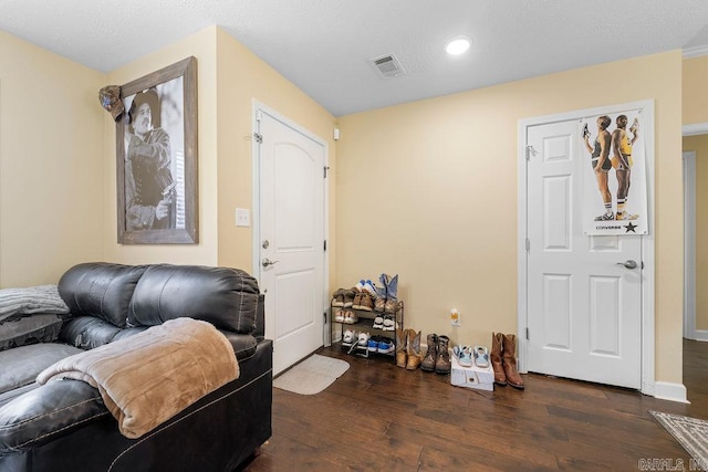 living area with a textured ceiling, wood finished floors, visible vents, and baseboards