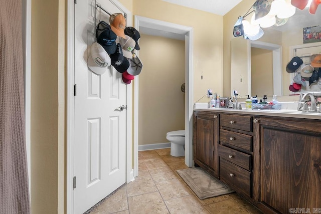 bathroom featuring double vanity, toilet, baseboards, and a sink