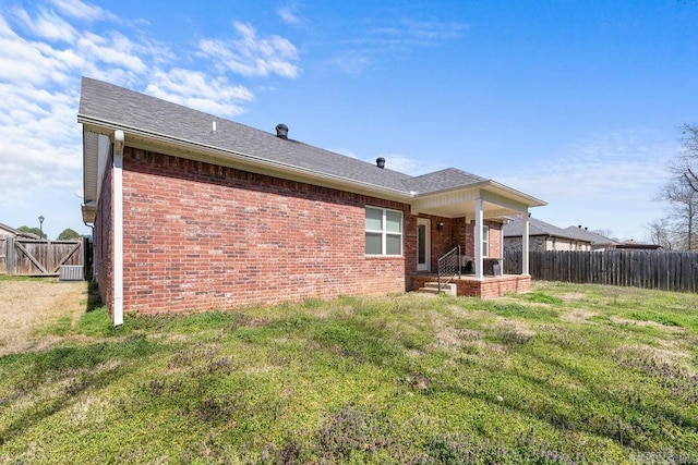 back of house featuring brick siding, a lawn, central AC, and fence