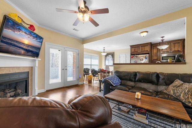 living room featuring wood finished floors, visible vents, ceiling fan, a textured ceiling, and crown molding