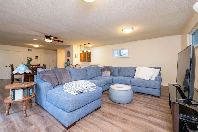 living room featuring visible vents, a textured ceiling, light wood-type flooring, and a ceiling fan