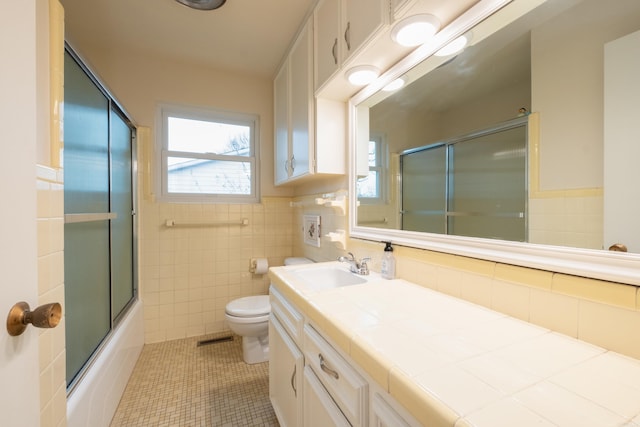 full bathroom with toilet, tile walls, tile patterned flooring, bath / shower combo with glass door, and vanity