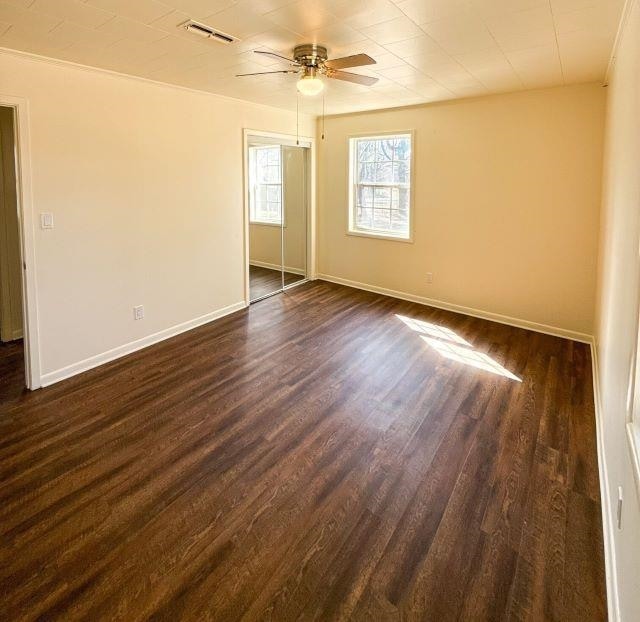 unfurnished bedroom featuring dark wood-type flooring, baseboards, visible vents, and a closet