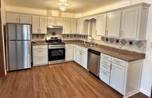 kitchen featuring under cabinet range hood, dark countertops, appliances with stainless steel finishes, and dark wood-style flooring