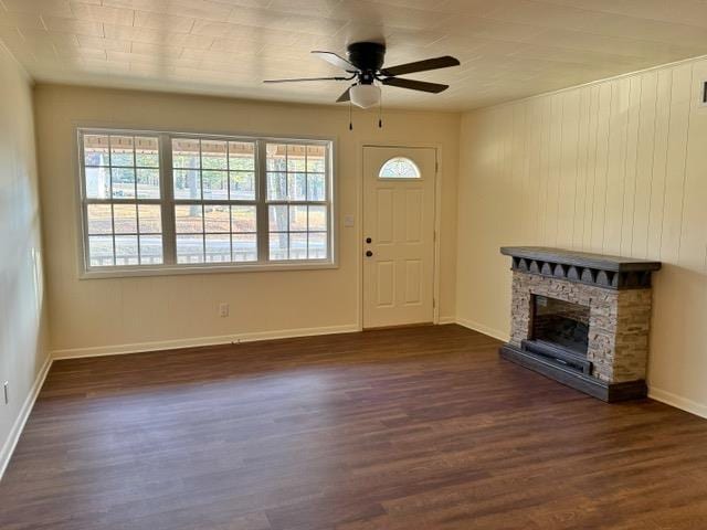 foyer with a stone fireplace, baseboards, dark wood-type flooring, and a ceiling fan