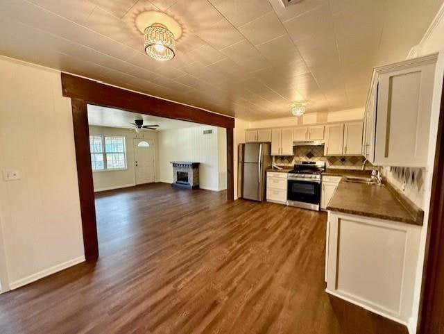 kitchen with dark countertops, a sink, under cabinet range hood, appliances with stainless steel finishes, and dark wood-style flooring