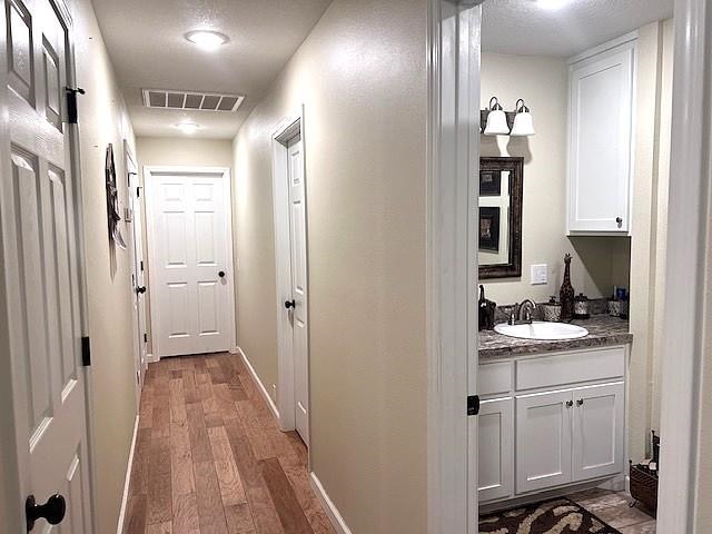 hall with visible vents, wood finished floors, baseboards, and a sink