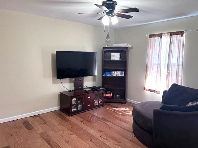 living area with a ceiling fan, wood finished floors, and baseboards