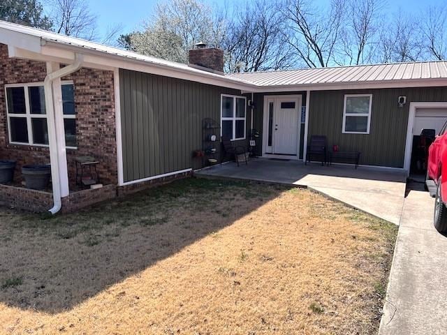 rear view of property featuring metal roof, a yard, a chimney, and a patio area