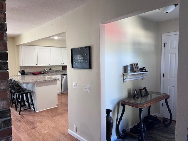 kitchen featuring a peninsula, dishwasher, light wood-style floors, white cabinetry, and a kitchen breakfast bar