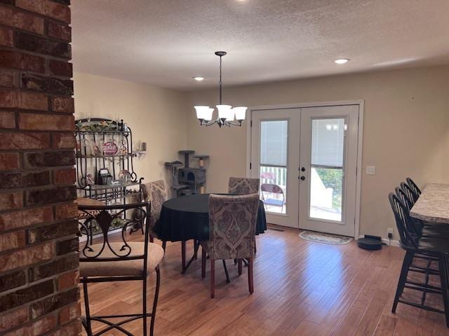 dining room with a textured ceiling, wood finished floors, french doors, baseboards, and a chandelier