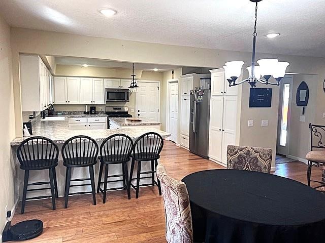 kitchen featuring a breakfast bar area, a peninsula, an inviting chandelier, light wood-style floors, and stainless steel appliances