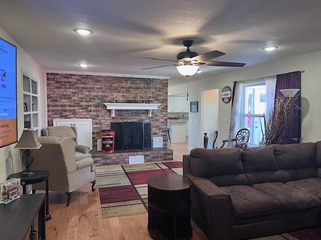 living area with built in features, a fireplace, light wood-type flooring, and ceiling fan