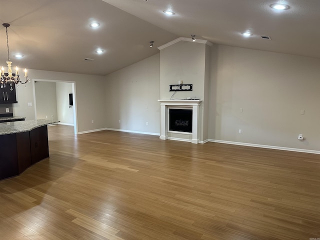 unfurnished living room featuring visible vents, an inviting chandelier, lofted ceiling, a fireplace, and light wood-style floors