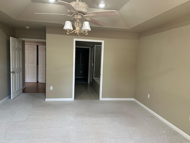 unfurnished bedroom featuring a ceiling fan, baseboards, carpet floors, ensuite bathroom, and a raised ceiling