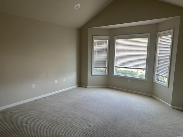 empty room with light colored carpet, baseboards, and vaulted ceiling