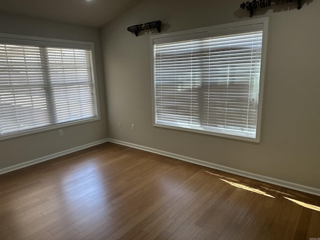 empty room with baseboards, lofted ceiling, and wood finished floors