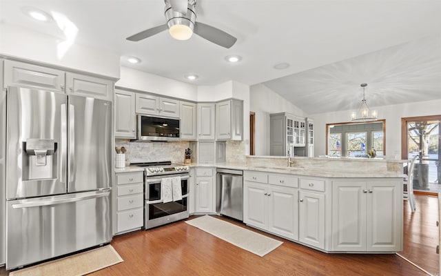 kitchen featuring a sink, backsplash, wood finished floors, stainless steel appliances, and a peninsula