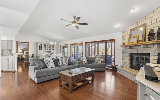 living area featuring dark wood-style floors, a fireplace, vaulted ceiling, and ceiling fan with notable chandelier