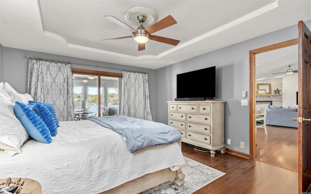 bedroom with access to exterior, a tray ceiling, dark wood-style floors, baseboards, and ceiling fan