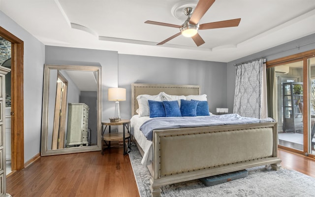 bedroom featuring access to exterior, a tray ceiling, wood finished floors, and ceiling fan