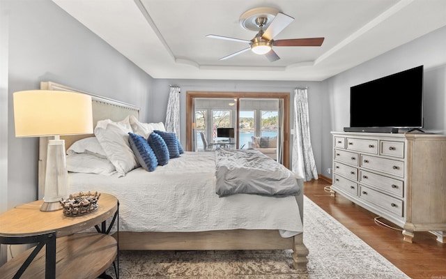 bedroom with a ceiling fan, a tray ceiling, access to outside, and dark wood-style floors