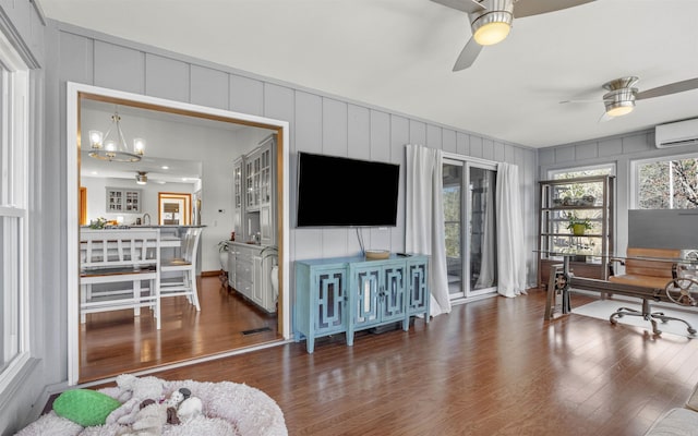 office space featuring a wall mounted air conditioner, wood finished floors, and ceiling fan with notable chandelier