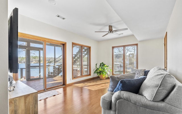 living room featuring a ceiling fan, visible vents, light wood finished floors, and baseboards