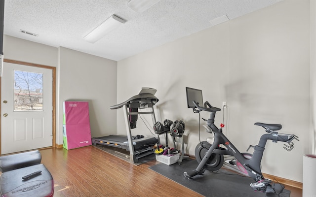 exercise area with visible vents, a textured ceiling, and wood finished floors